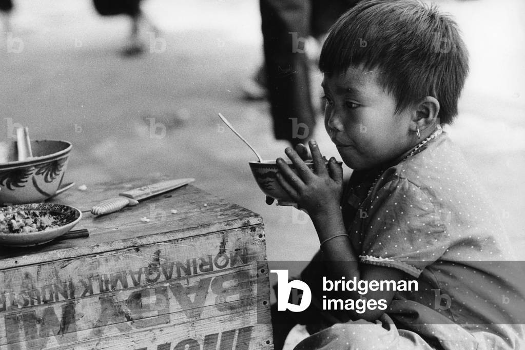 A Vietnamese small child eating in a street, 1968 (b/w photo)