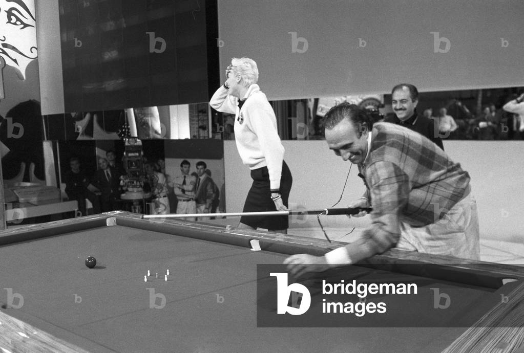 Italian TV host Pippo Baudo playing pool with Brigitte Nielsen, Italy, 1987 (b/w photo)