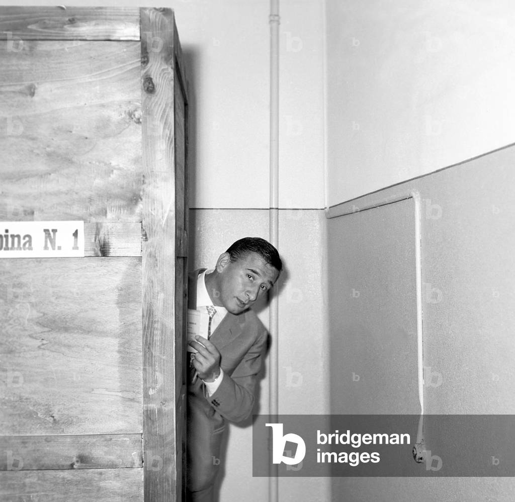 Renato Rascel peeping out from the polling box, Italy, 1954 (b/w photo)
