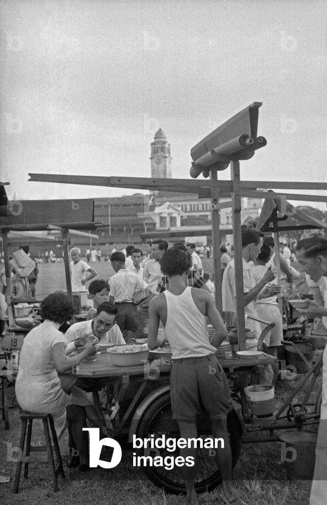 People eating street food sitting at a kiosk, Singapore, 1962 (b/w photo)