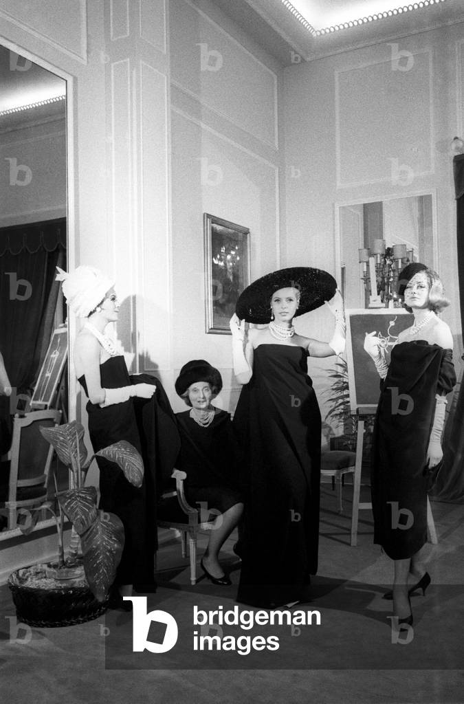 Biki poses sitting in front of a mirror behind three models