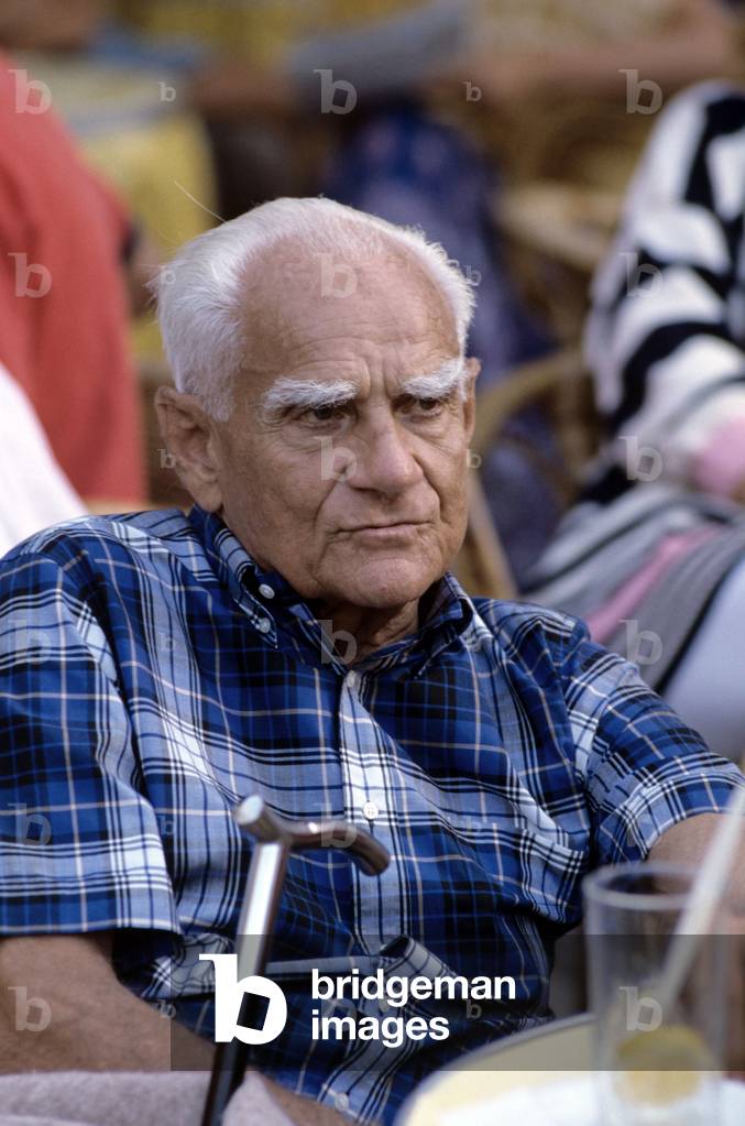 Alberto Moravia sitting at a café small table