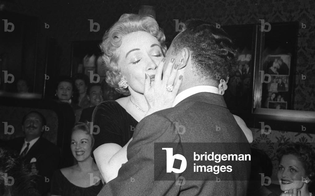 Marlene Dietrich kissing singer Billy Daniels, and her daughter, Maria Riva, in the background, Stork Room, London, UK, 1956 (b/w photo)
