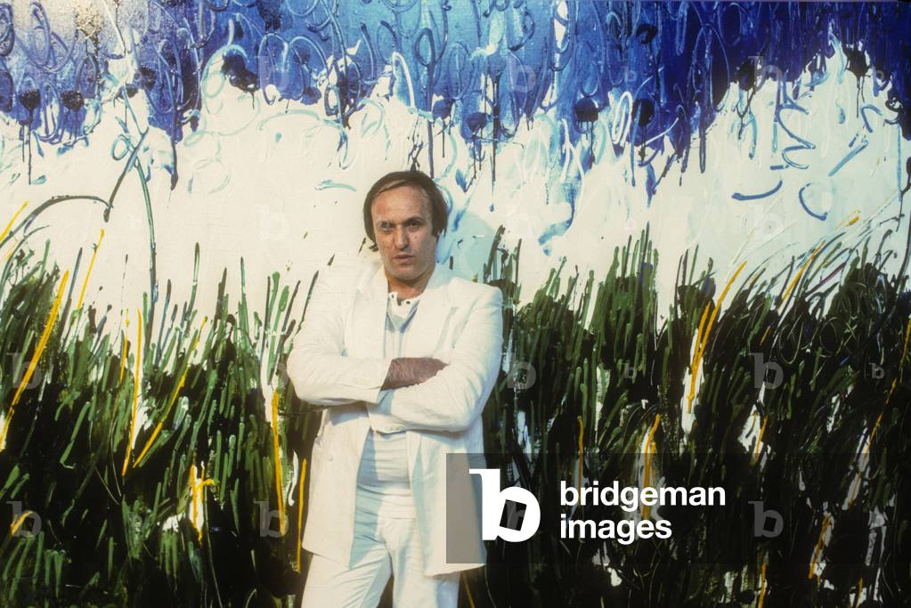 Venice, 1984. Italian artist Mario Schifano in front of one of his paintings