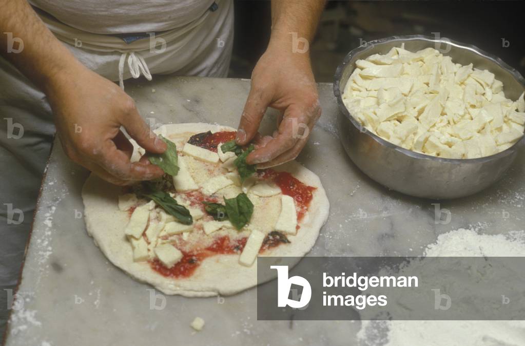Naples, Italy. Preparation of Pizza Margherita at Brandi pizza restaurant, where in 1889 it was invented in honour of Queen Margaret (Margherita) of Savoy. Fifth step: sprinkle with Mozzarella cheese