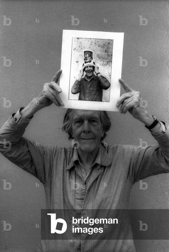 Portrait of composer and poet John Cage, holding a photo of him from 1983 representing him holding a photo of him in 1982, by abime, Perugia, Italy. 1992.