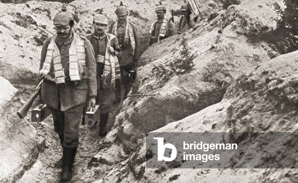 German soldiers wearing spiked helmets and carrying ammunition cartridges around their necks walking along a trench during World War One, from The Pageant of the Century, pub.1934