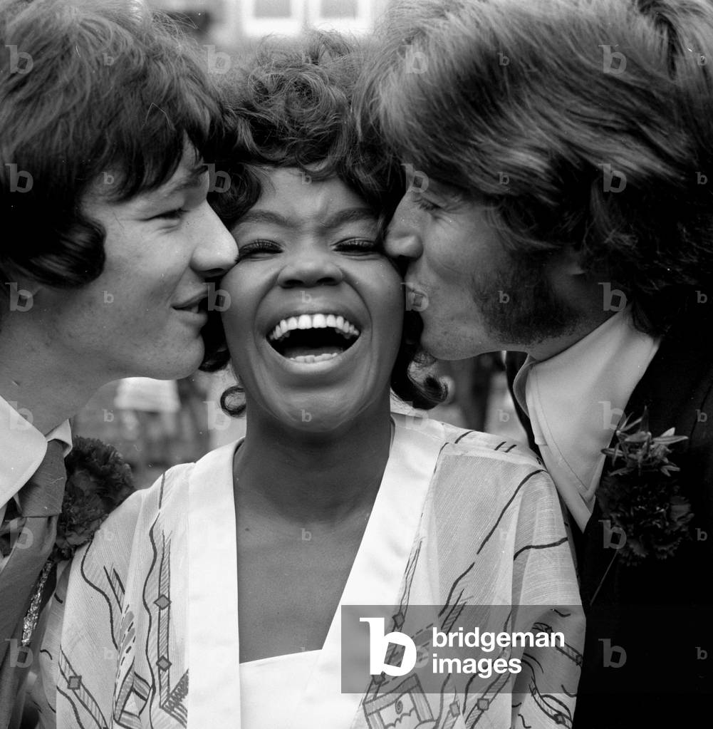 American Pop singer P.P. Arnold receives a kiss from her new husband, manager Jim Morrison (left) and Barry Gibb of the Bee Gees pop group on her wedding day October 1968 (b/w photo)