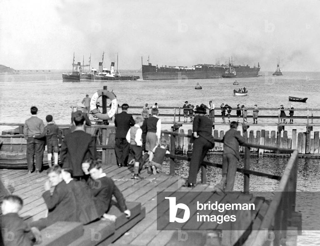Spectators watch from the banks of the River Tyne as the hull of the Former Crack liner ship Olympic leaves Jarrow bound for Inverkeithing, where her breaking up will be completed, c. 1930