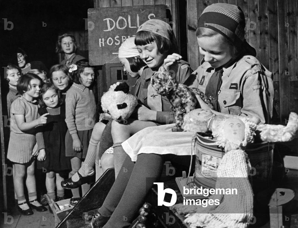 A toy for every child in this village, from a dolls hospital. Stella West, Paddy Brown, and Gwen Lidbetter- three village girls of Storrington, Sussex, are working hard to do this. Attics and lofts have been searched for old broken toys and dolls, and they are taken to the dolls hospital at the Brownie Pack H.Q. here the three get to work sewing, painting, and repairing, making them as good as new. November 1942 (b/w photo)
