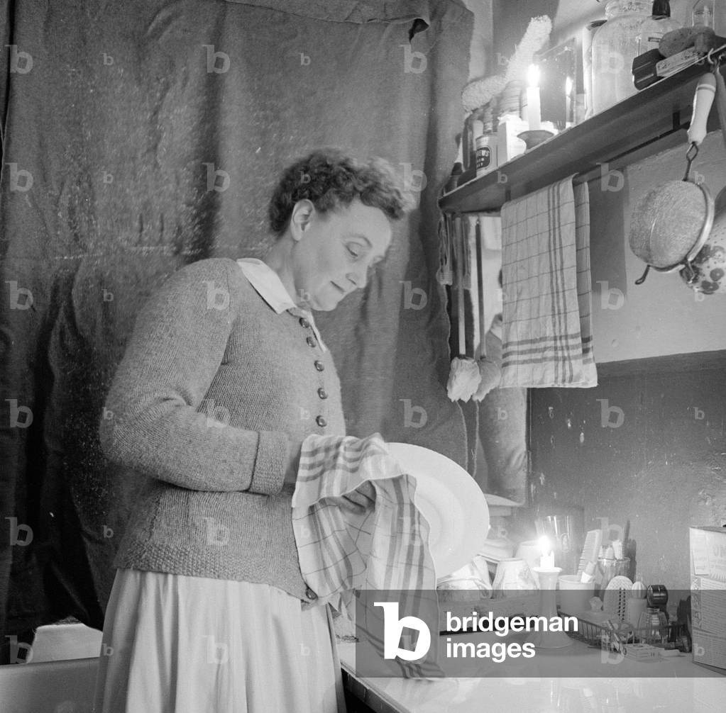 Mrs Dorothy Mead who still lights her house with gas lamps 
Seen here washing up by candle light
Circa 1958
