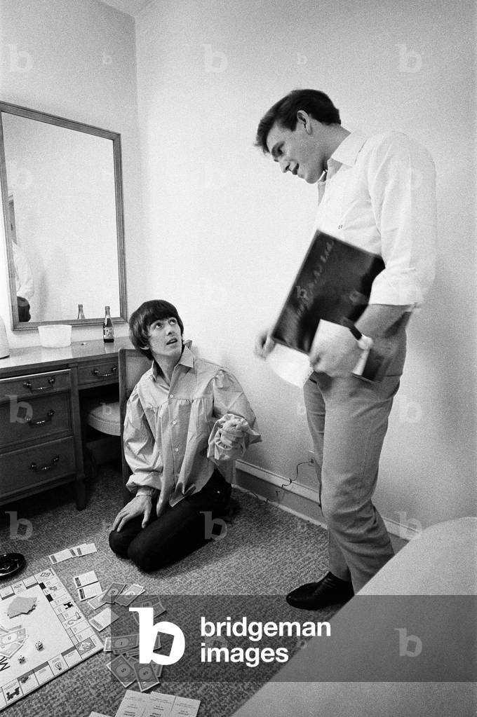 George Harrison speaks with Neil Aspinall while enjoying a game of Monopoly with singer songwriter Jackie de Shannon (not pictured), one of the tour's support acts, at the Lafayette Motor Inn, Atlantic City, New Jersey, USA, Sunday 30th August 1964 (b/w photo)