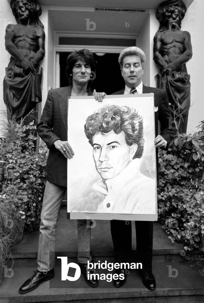 Rolling Stones: Ronnie Wood holds a painting of author Ken Follett who stands next to him. September 1987