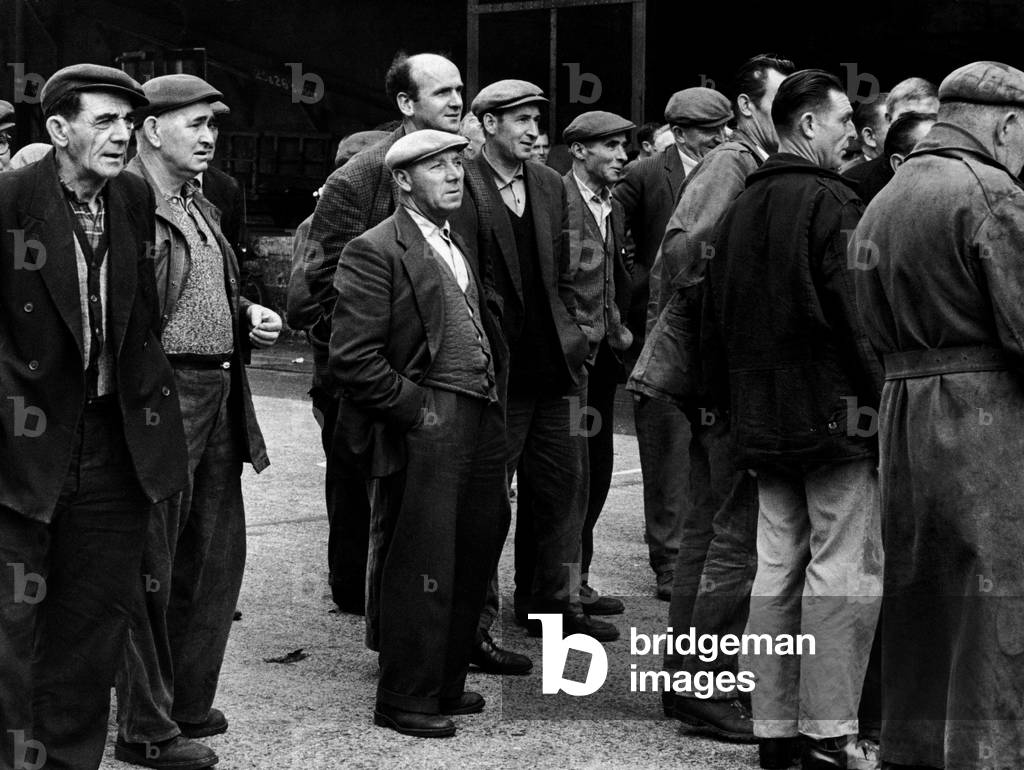 Peter Pearson, docker, of Seven kings-Ilford, starts his day at 6 am and finished at 7.30pm. The dockers assemble to await the allocation of work to their individual gangs. Peter is in the centre of the picture. 5th August 1965 (b/w photo)