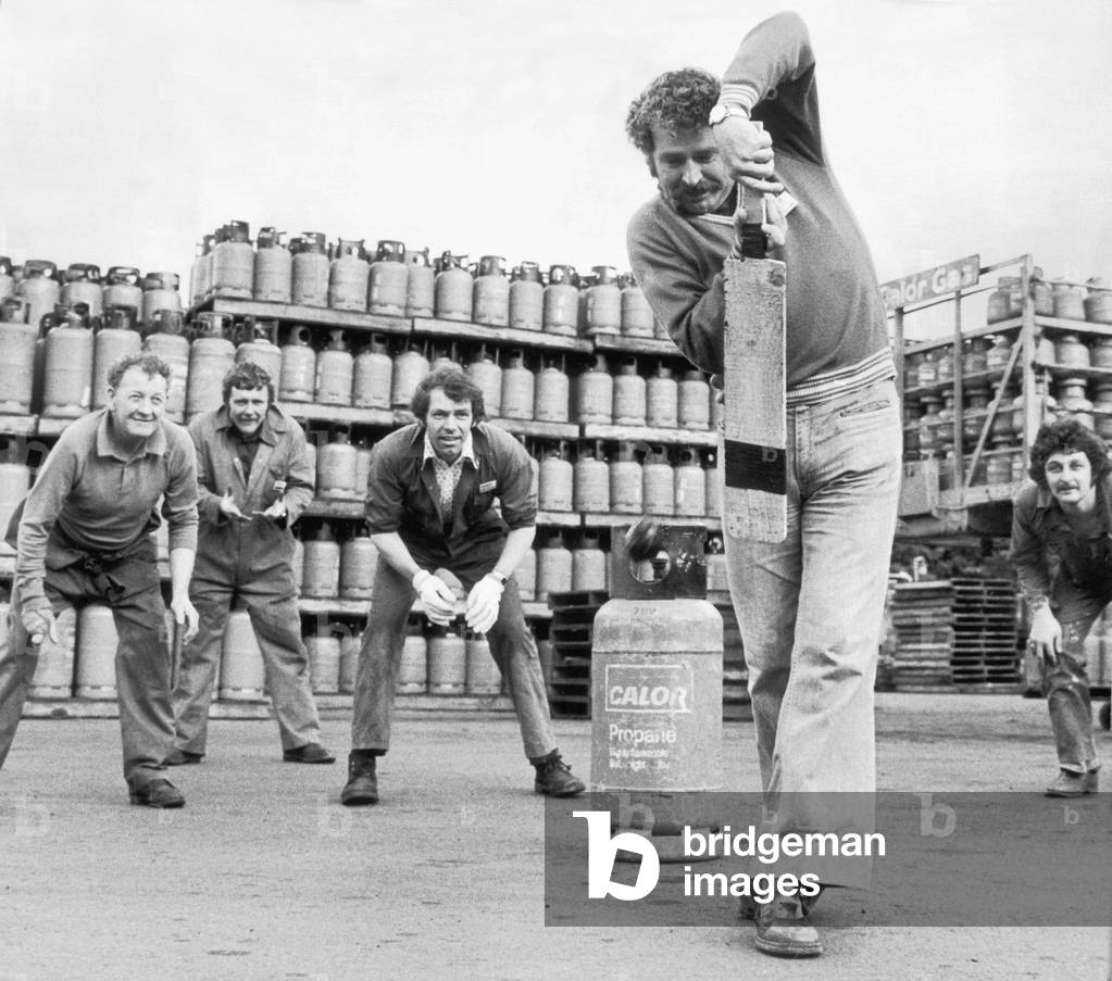 Geoffrey Williams, captain and opening batsman of Ynysgerwn Cricket club, keeps his eye in during break-time at work, in a bottle-gas depot at Aberdulais, Neath. He keeps score with gas bottles loaded on trailers, 23rd August 1979 (b/w photo)