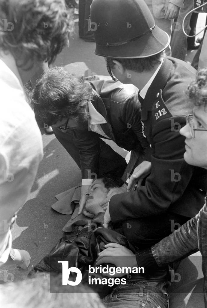 An injured rioter is cared for by a friend and a police officer in the centre of Lewisham. The riot was sparked by a National Front march through the centre of town, which was confronted by a left wing counter demonstration, August 1977 (b/w photo)