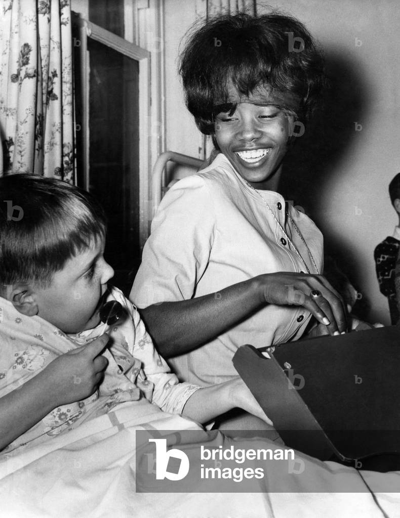 Millie Small sings her hit song My boy lollipop to William Entwhistle (5) during her visit to the children's ward at Burnley General hospital, May 1964 (b/w photo)