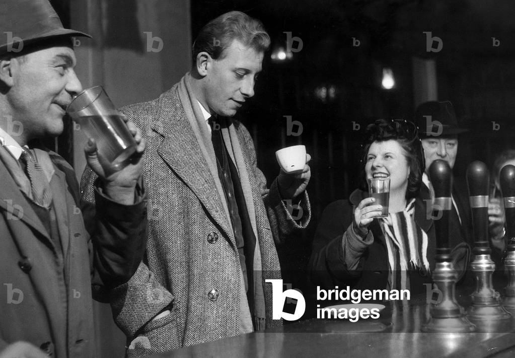Peter Woods a reporter on the Daily Mirror drinks a cup of coffee in a public house bar while all around him drink beer November 1954 (b/w photo)