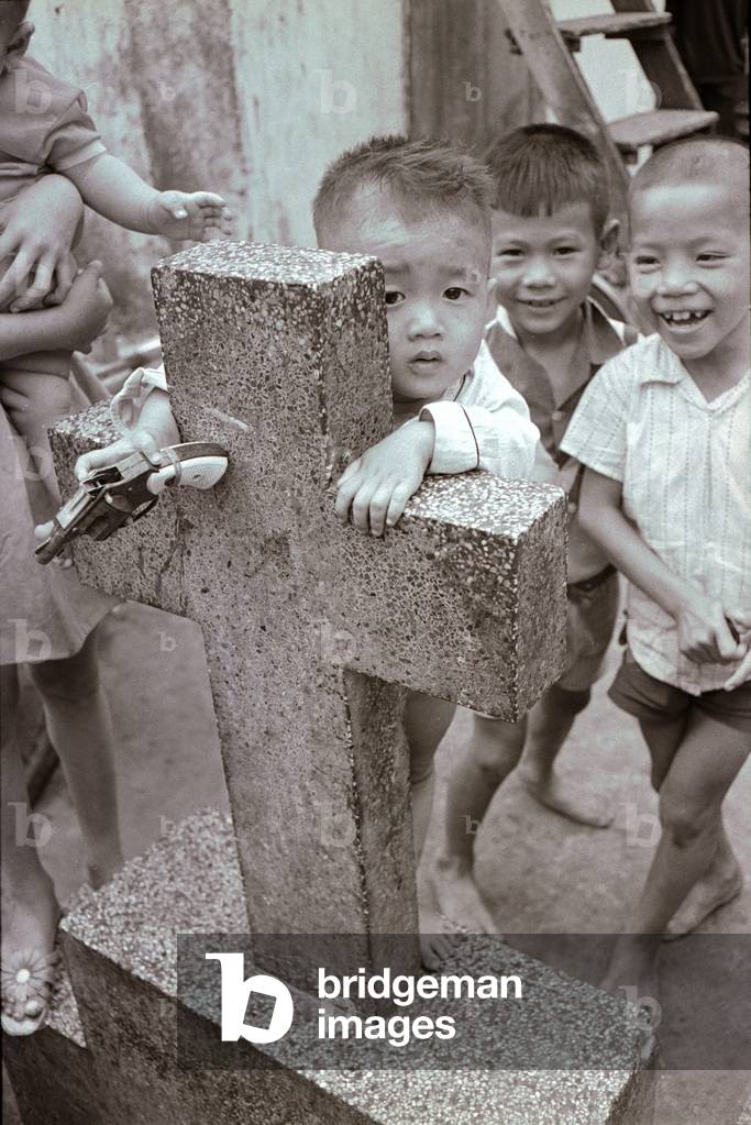 Three year old Thanh half naked on the grave of Marie Nguyen Thi Vong with a toy pistol in his hand, February 1970 (b/w photo)