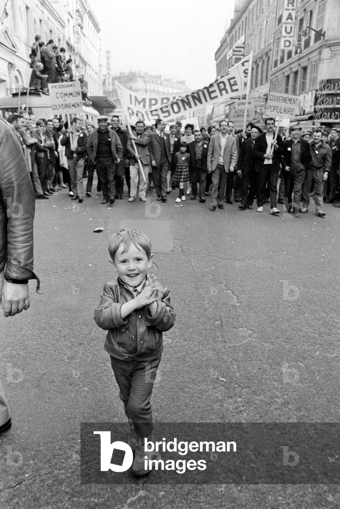 A small child walks in front of students and workers who are marching in demonstration in Paris prior to the June general election, June 1968 (b/w photo)