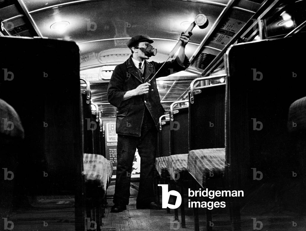 A cleaner seen here spraying a pesticide to kill germs during a routine cleansing of the bus at a London Transport garage, 30th May 1935 (b/w photo)