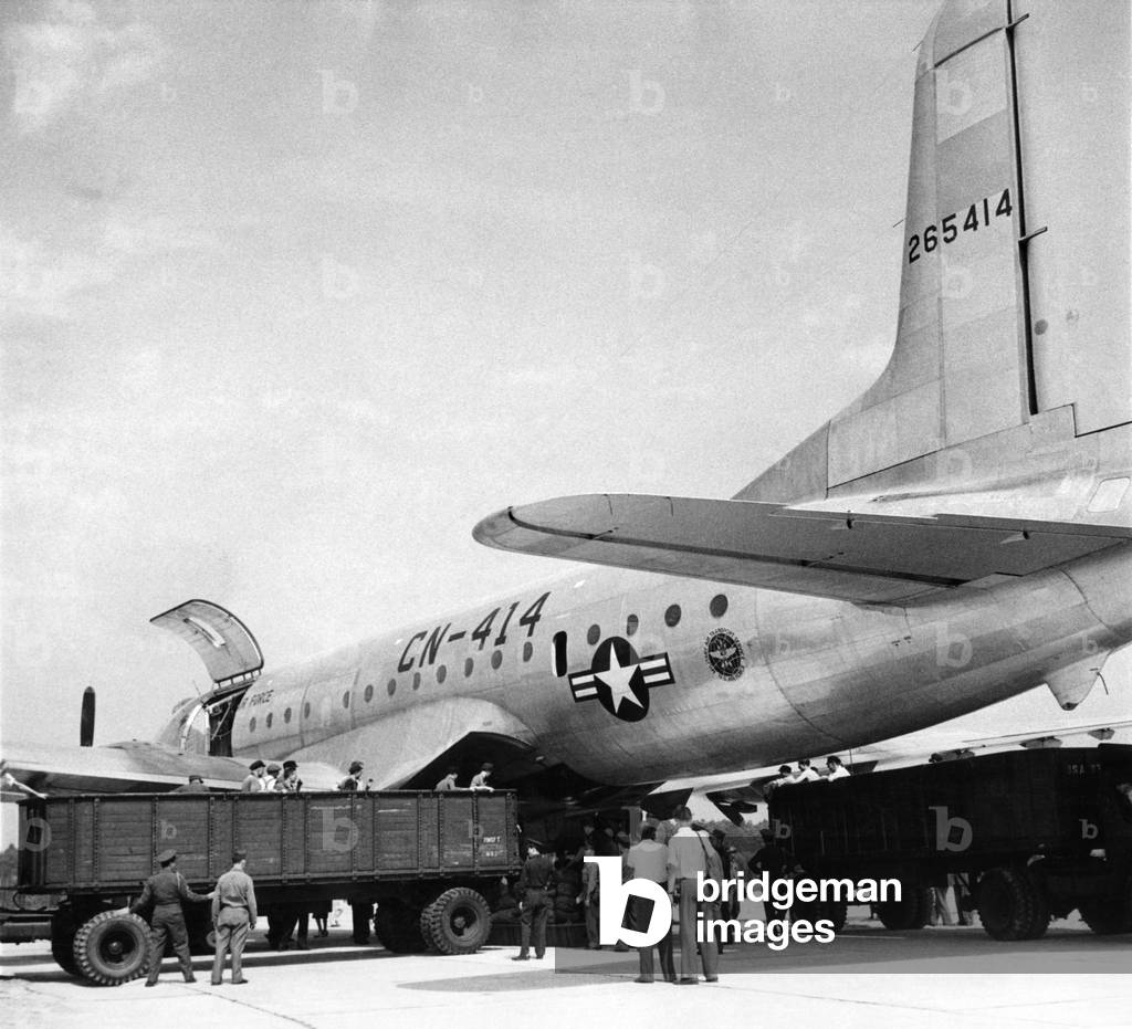 At Gatow Airport in Berlin where they are used to seeing bigger and better efforts every day, they took their hats off when the biggest air lift load of all time arrived in the world's largest transport plane, a Globe Master, of military air transport service of the U.S. Army air Force. It was unloaded in record time, trailer trucks being shunted from all sides as the huge belly of the aircraft opened up and disgorged its cargo. Berliners get a look at the work of unloading. August 1948