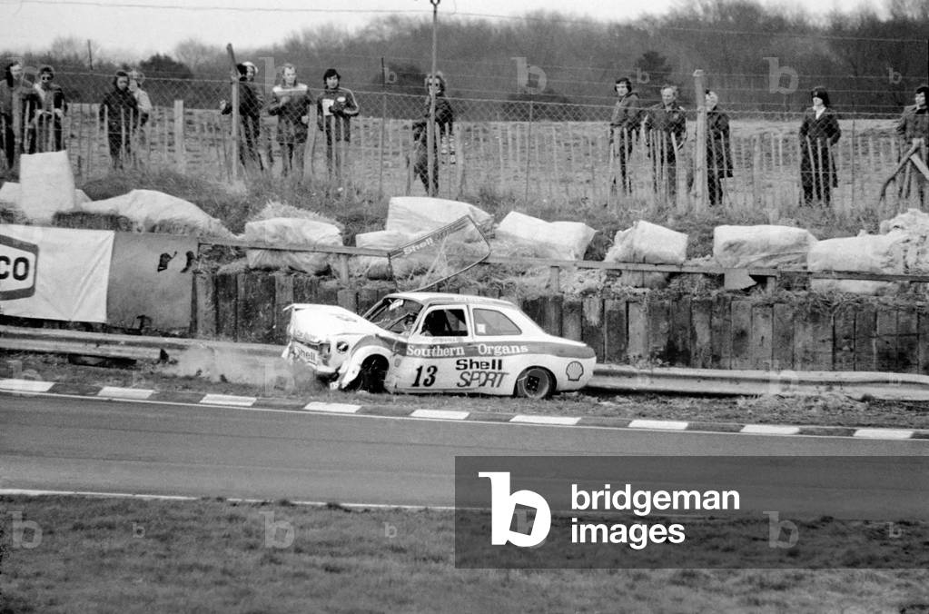 First race crunch for the snow Queen. Britain's ex-ski champion Divina Galica crashed her £6000 car on the second lap of her very first professional race at Brands Hatch today, 2nd February 1975 (b/w photo)