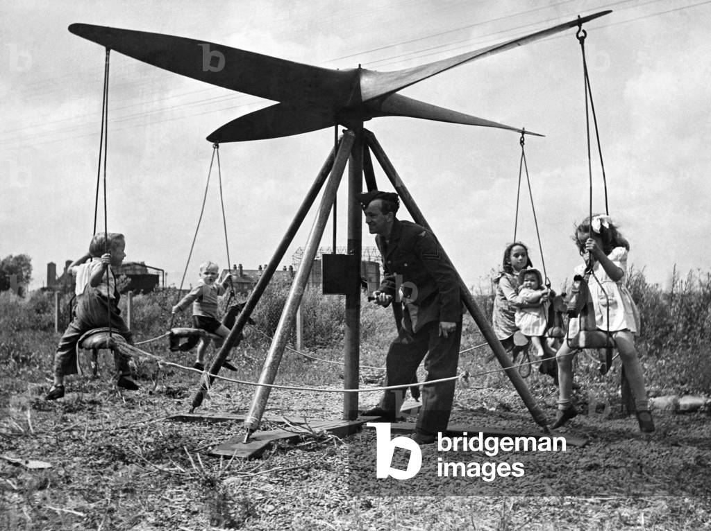 A airman operates a propeller roundabout. Seen here giving local children a ride. July 1946 P012160
