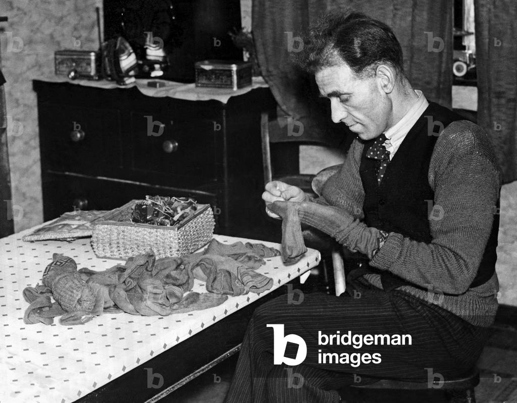 A Man sits at his table darning his socks, 10th February 1937 (b/w photo)