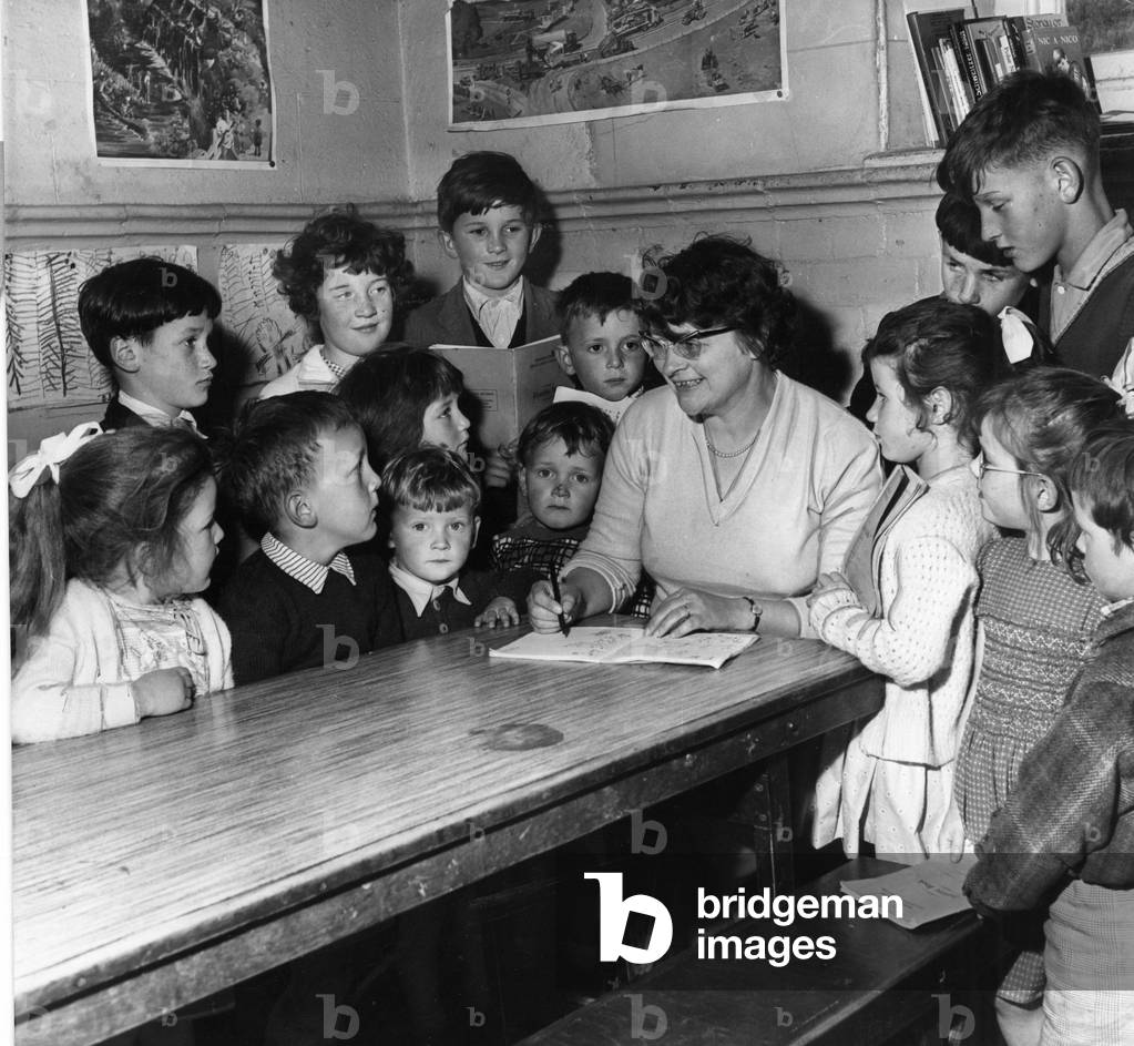 Tryweryn Valley - Mrs Martha Roberts marks the books of her young pupils in the one room school, at Capel Celyn, first opened in 1881. The valley is to be flooded for a reservoir, July 1963 (b/w photo)