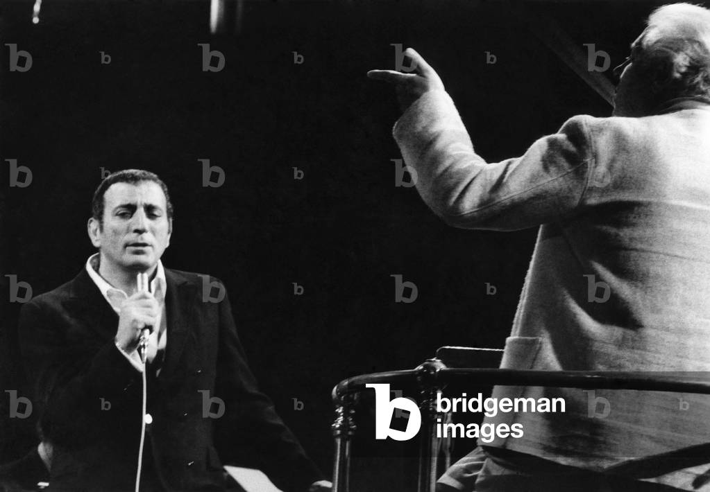 Tony Bennett In London Concert. American singer Tony Bennett starred in a concert with the London Philharmonic Orchestra at London's Royal Albert Hall on Sunday (31-1-71). Wielding the baton at the charity concert, in aid of the L.P.O. appeal fund, was Bennetts friend Robert Farnon. The first part of the concert was devoted to light classical music written by Farnon. In the second half, Bennett sang twenty of his hit songs, backed by 90 musicians: the entire L.P.O. less its woodwind section, combining with 15 of London's leading jazz players. Tony Bennett rehearsing for his concert at the Albert Hall. 31st January 1971 (b/w photo)