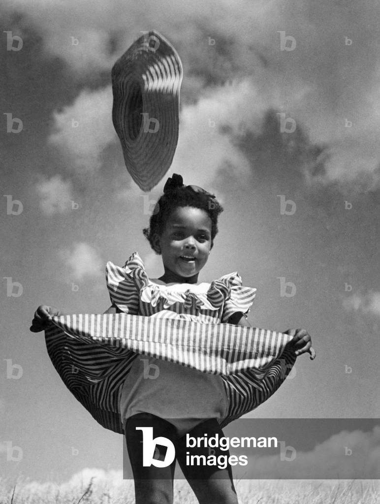 Little child wearing candy stripped dress is caught by the wind and way goes the sun bonnet. c, 1949 (b/w photo)