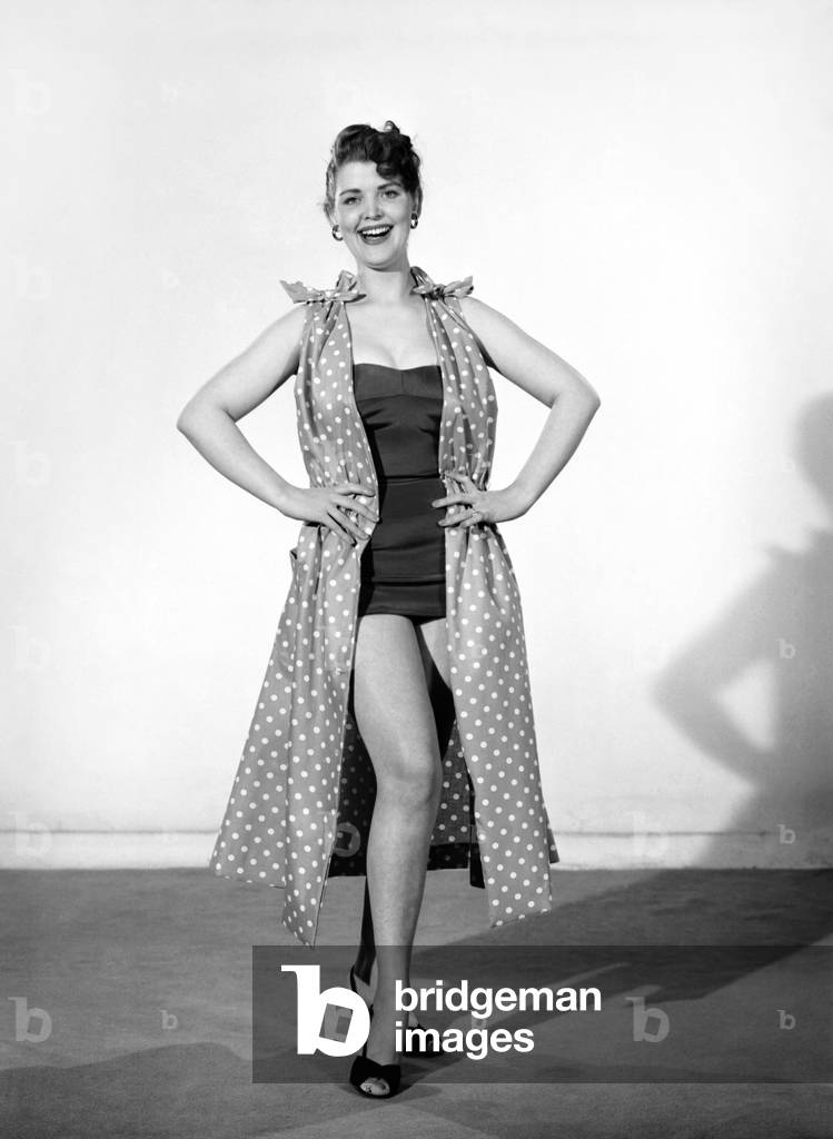 Clothing: Fashion: Beachwear: Woman wearing beach wrap and dress. Model: Audrey Hurst. 1955 (b/w photo)