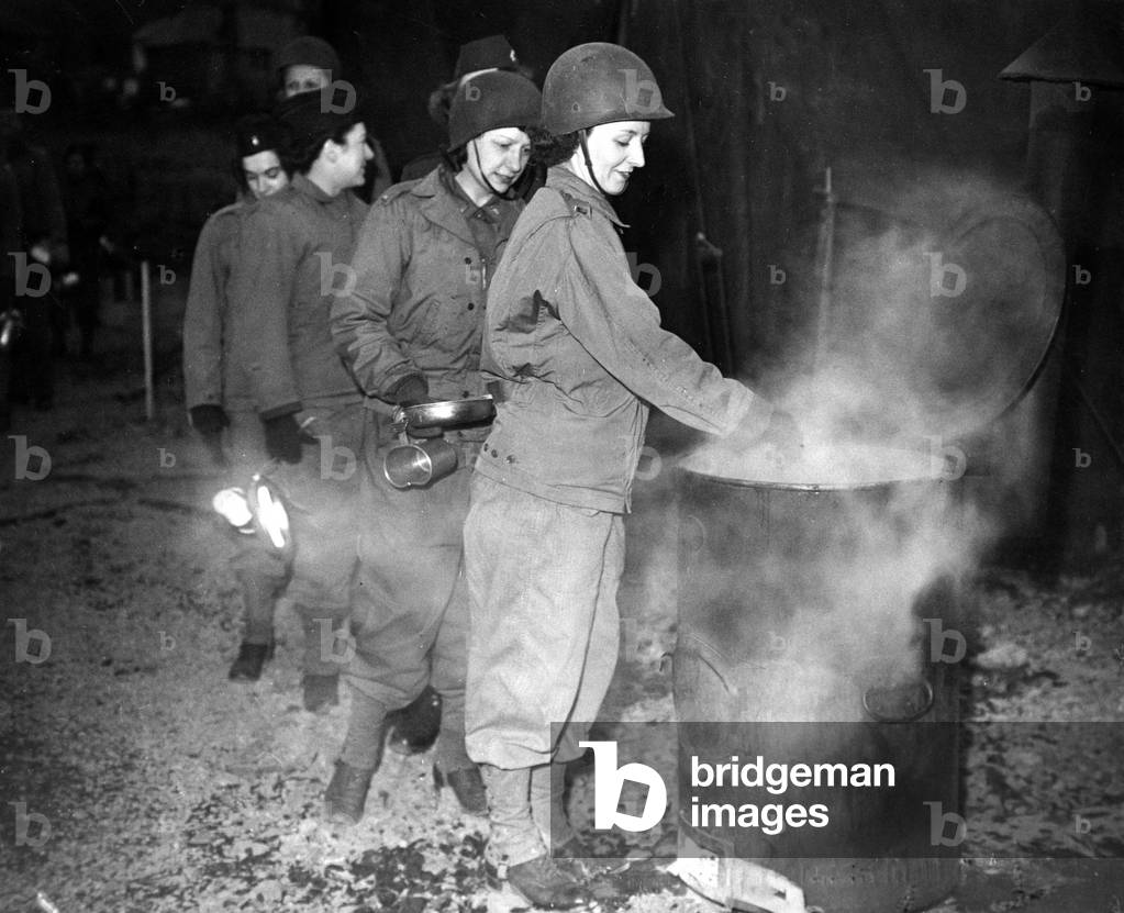 Women of a US Army nursing unit queue up with plates and mugs while camping in Wales to receive their food which is cooking in a giant tin, 24th February 1944 (b/w photo)