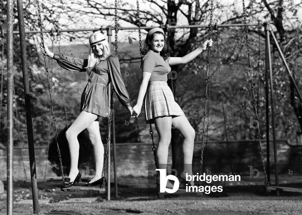 Two teenage sisters playing together on a swing in the local park. November 1969
