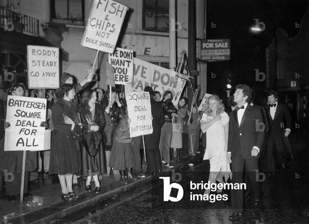 A couple arriving for the opening-night party of the new club belonging to Roddy Llewellyn, run the gauntlet of jeering demonstrators, April 1978 (b/w photo)