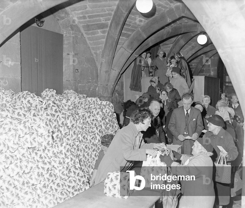 Seasonal goodwill and cheer began for hundreds of old age pensioners in Coventry today when the distribution of 8,500 parcels from the Lord Mayor's Christmas Fund started in the crypt of St. Mary's Hall in Bayley Lane. Each of the pensioners filed through the building to receive one of the parcels which contained 15 grocery items pakced in gay carrier bags. The bag included a Christmas pudding, tea, sugar, biscuits, tins of steak, chicken, sardines, salmon, cream and fruit. The Lord Mayor, Alderman W. Parfitt, was there to give a Christmas greeting to the first few hundred arrivals and to hand them personally an envelope containing a Christmas card and 2s. 6d. 