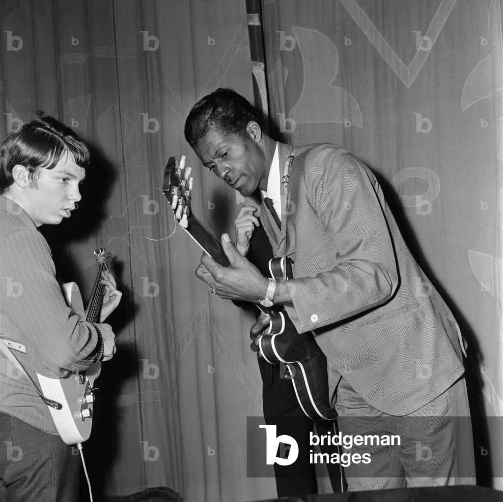 American rock and roll singer and musician Chuck Berry tunes up his guitar before going on stage to give a show at a Manchester cinema. 12th January 1965 (b/w photo)