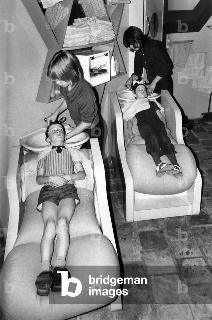 A Haircut and Baked beans on Toast, please! Two youngsters take their hair beauty treatment lying down, at Meenys in Kensington. September 1971