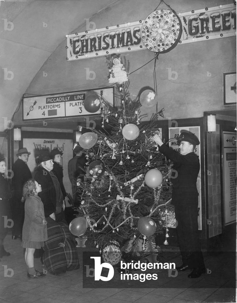 An underground railway guard decorating a Christmas tree at Holburn tube station, 9th December 1940 (b/w photo)