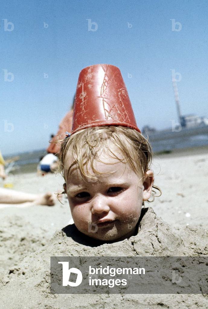 Summer holidays July 1976 - Boy buried in sand with red plastic Bucket on his head
