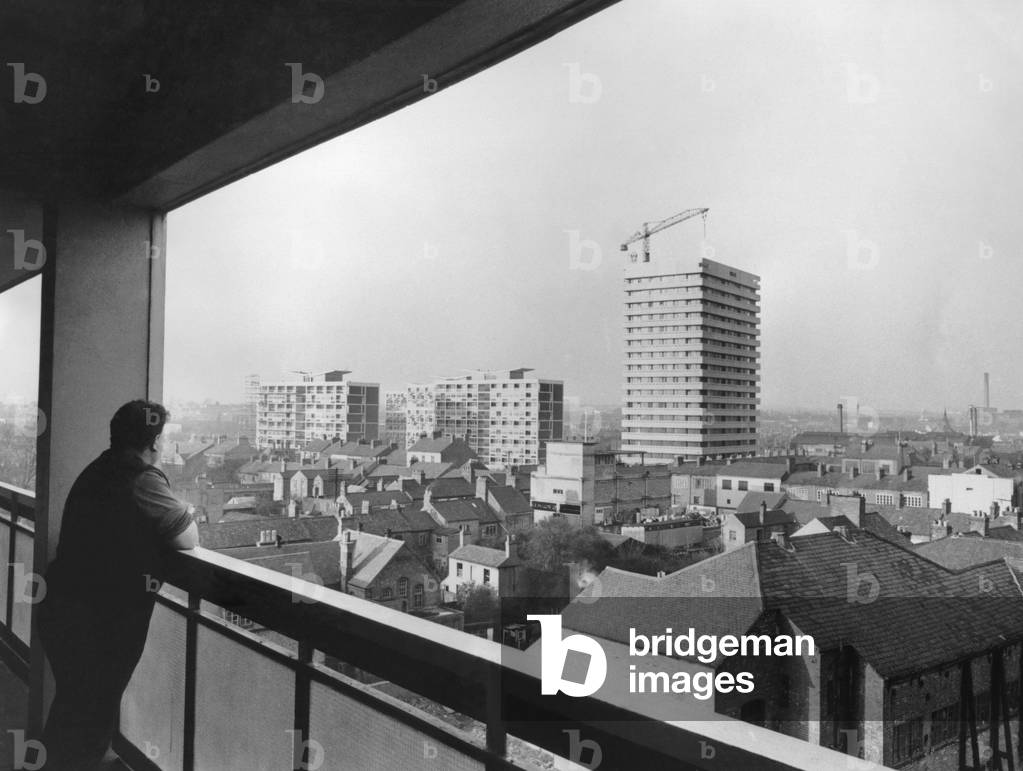 A resident on the eighth floor of Hillfields House, in Yardley Street, Coventry, looks out over the roofs of Hillfields at new flats rising up in Castle Street.
1st December 1966