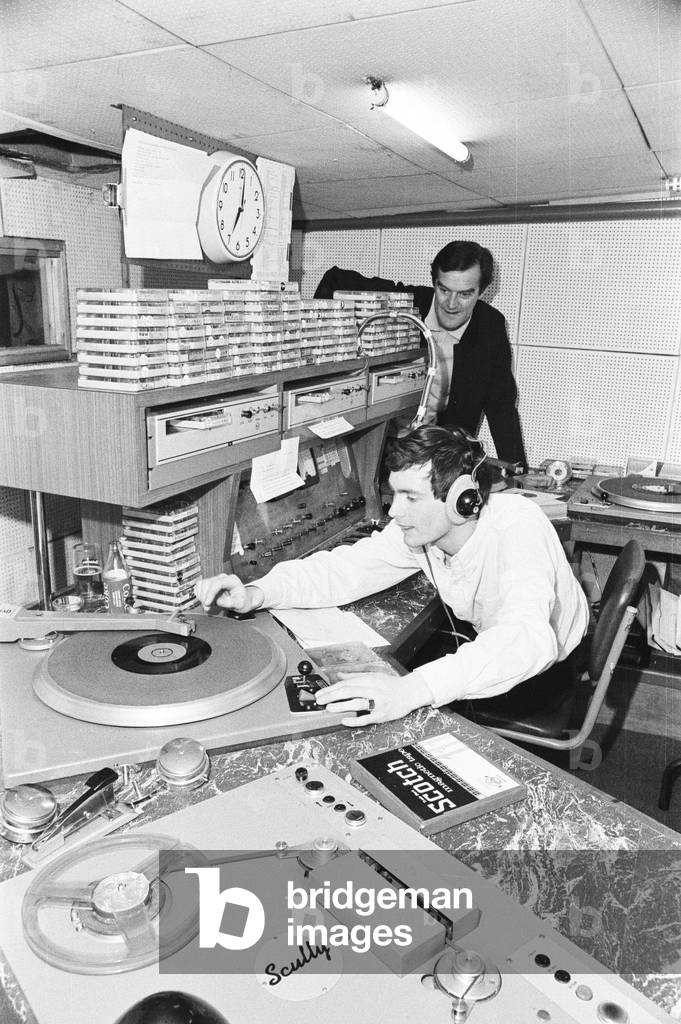 Radio London, offshore commercial radio station, which operated from 23rd December 1964 to 14th August 1967, from a ship, MV Galaxy, anchored in the North Sea, also know as a pirate radio station. 28th July 1966. Pictured, in studio, DJ Kenny Everett signs off at 7pm, watched by Tony Windsor, 1966 (b/w photo)