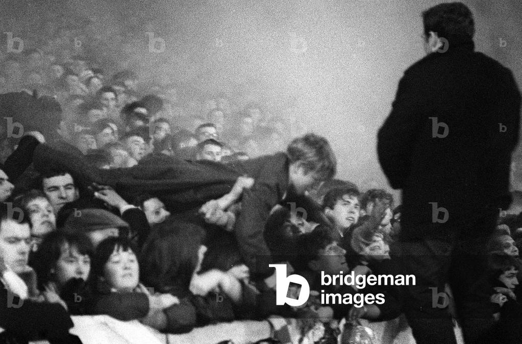 European Cup Second Round Second Leg match at Anfield. Liverpool 2 v Ajax 2 (Amsterdam win 7-3 on aggregate). Police and St John's ambulance worlers tend to dazed and injured spectators who were pushed onto the pitch from the Kop as fans pressed forward for a better view of the action in the low hanging fog. Here a child is being helped out from the crowd. More than 200 were injured in the crush. 14th December 1966 (photo)