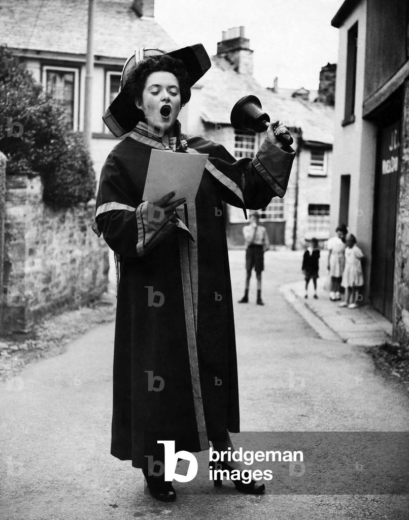 Here's the town crier - a 1943 version - the girl on the crier's arm used all her charm to be allowed to wear his regalia (you know what women are!) and beneath his civic dignity, and his stentorian voice, he has a soft heart - he allows the girl to wear the regalia, and try out her voice with the aid of the bell. Plymouth, 2nd August 1943 (b/w photo)