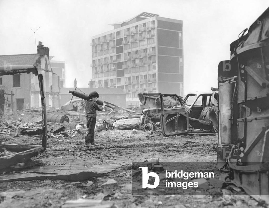 A small boy rummages among the tangled wrecks of old cars on waste ground in the Hillfields area of Coventry. In the background is the towering block of flats in Queen Street.4th February 1965