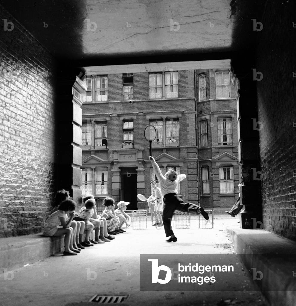 Inspired by the Wimbledon tennis championships taking place, these children enjoy a game of tennis in the back streets around their home in South East London. 9th July 1961 (b/w photo)