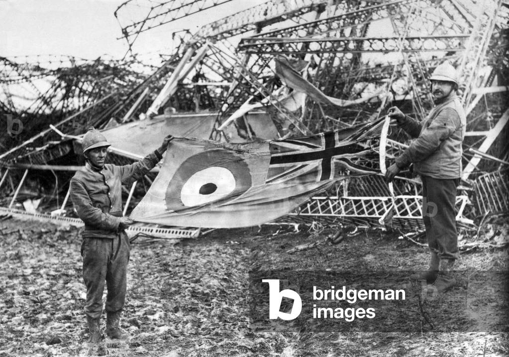The wreckage of the R101 airship which crashed at AAllonne, Beauvais, near Paris, France. Firemen holding up the scorched ensign, which was found flying at the stern. 5th October 1930.