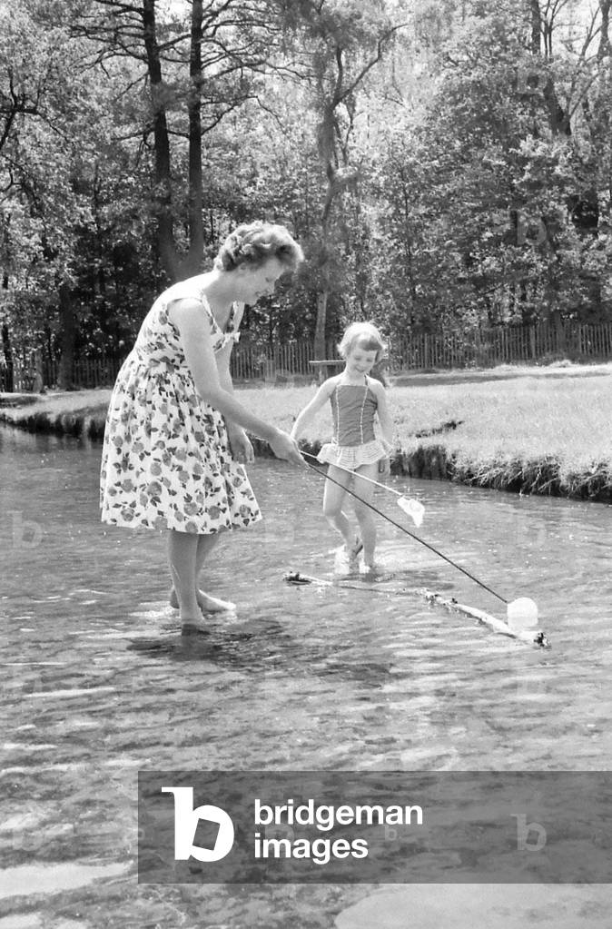 A little girl splashes away with her mother in a stream just inside the main gate of Sutton Park, 29th July 1962 (b/w photo)