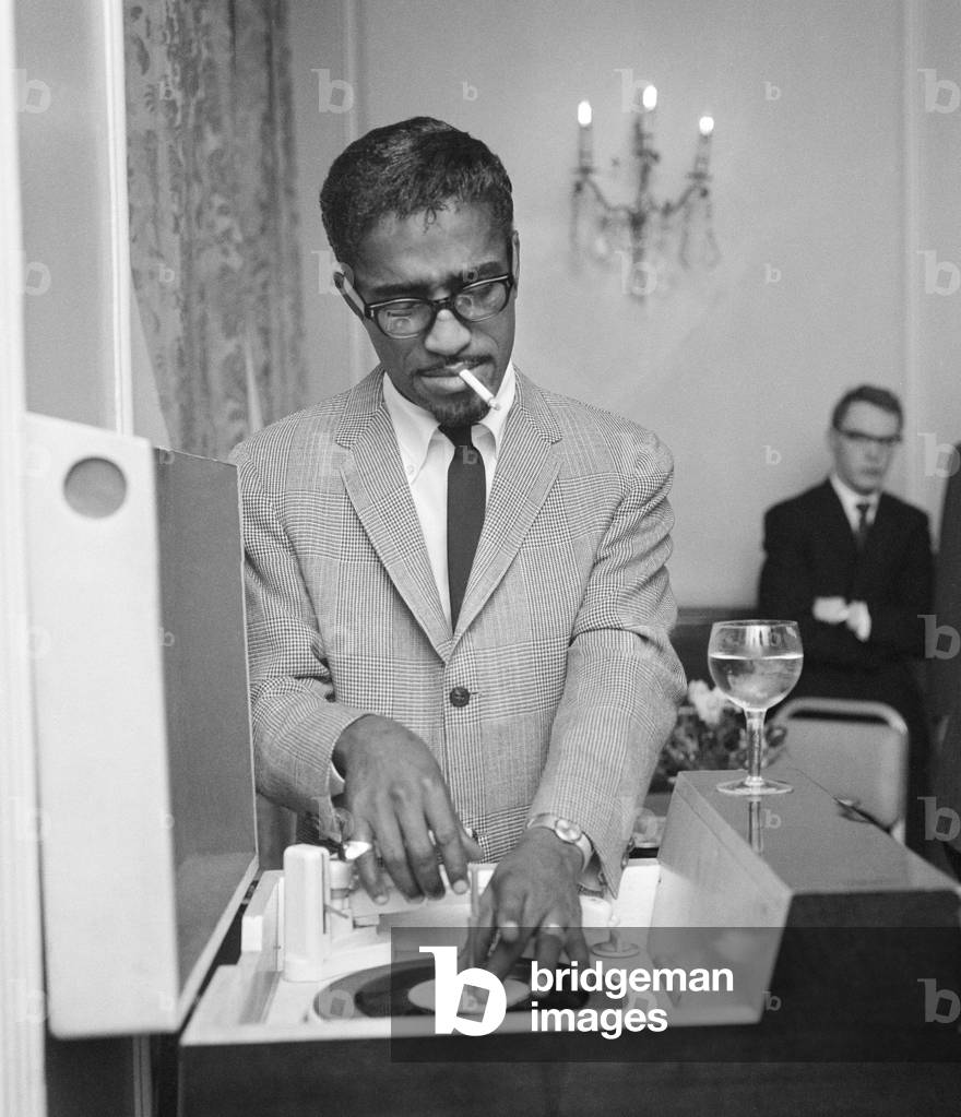 American singer Sammy Davis Jnr. puts on a record in a London restaurant whilst having lunch with friends. 7th May 1962 (b/w photo)